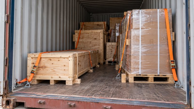 Peti dan kardus dengan ukuran berbeda tersusun di dalam container menggunakan penahan muatan.